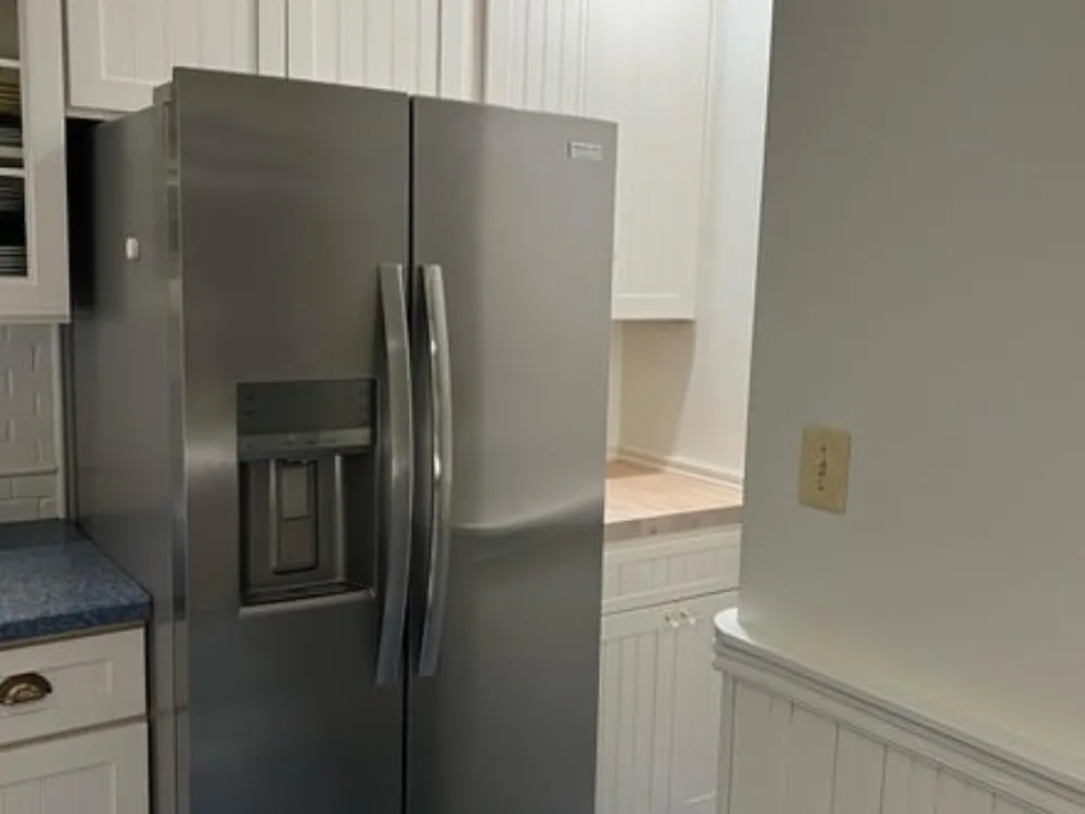 Drywall installation for simple kitchen with clean white walls and paneling around a stainless steel refrigerator and built-in cabinetry.