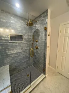 Modern walk-in shower with blue subway tiles, brass fixtures, and marble bench from a Full Bathroom Renovation project.